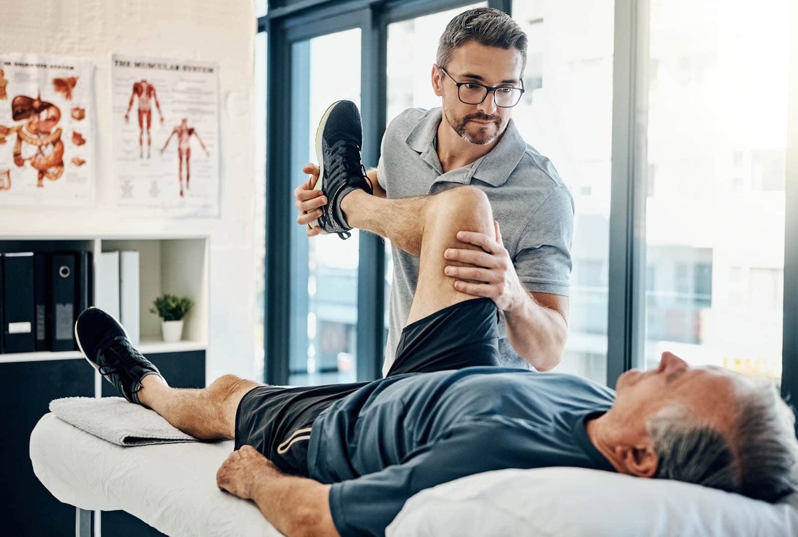 Physiotherapeut führt eine Beindehnungsübung mit einem älteren Patienten durch, Demonstration von Techniken aus einer Weiterbildung für Physiotherapeuten.